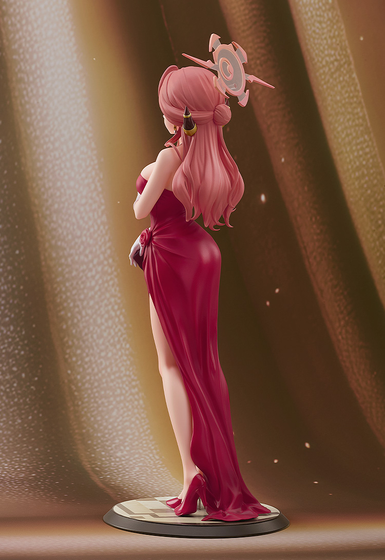 Figurine of a character with pink hair and a red dress against a brown curtain background