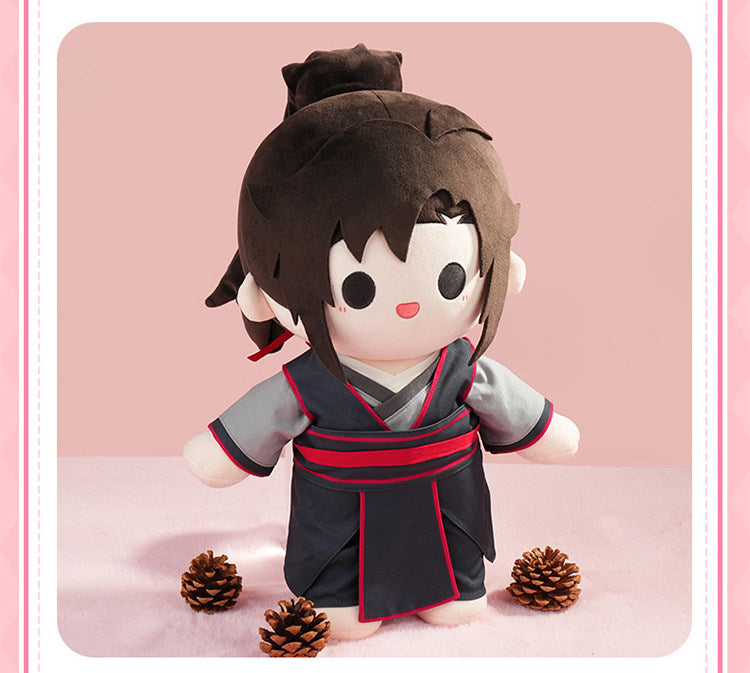 A chibi-style plush doll with dark brown hair, a white face and arms, and a dark navy outfit with red trim, standing on a pink surface against a pink background with three pinecones around it.