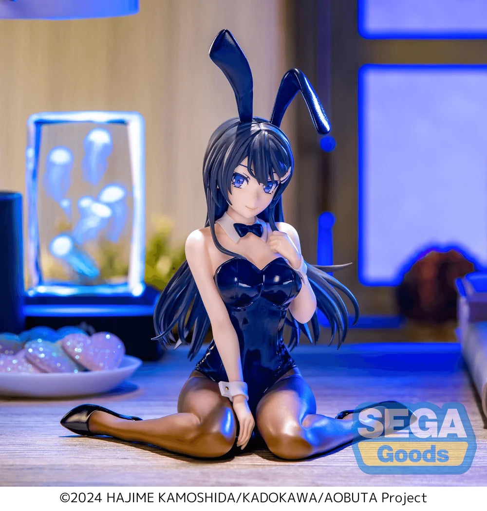 A seated anime-style collectible figure with long black bunny ears, a glossy black bunny outfit, and black thigh-high stockings, posed on a wooden surface in a blue-lit room. A SEGA Goods logo appears in the lower right, and a copyright line for the Hajime Kamoshida/Kadokawa/Aobuta Project is printed along the bottom.