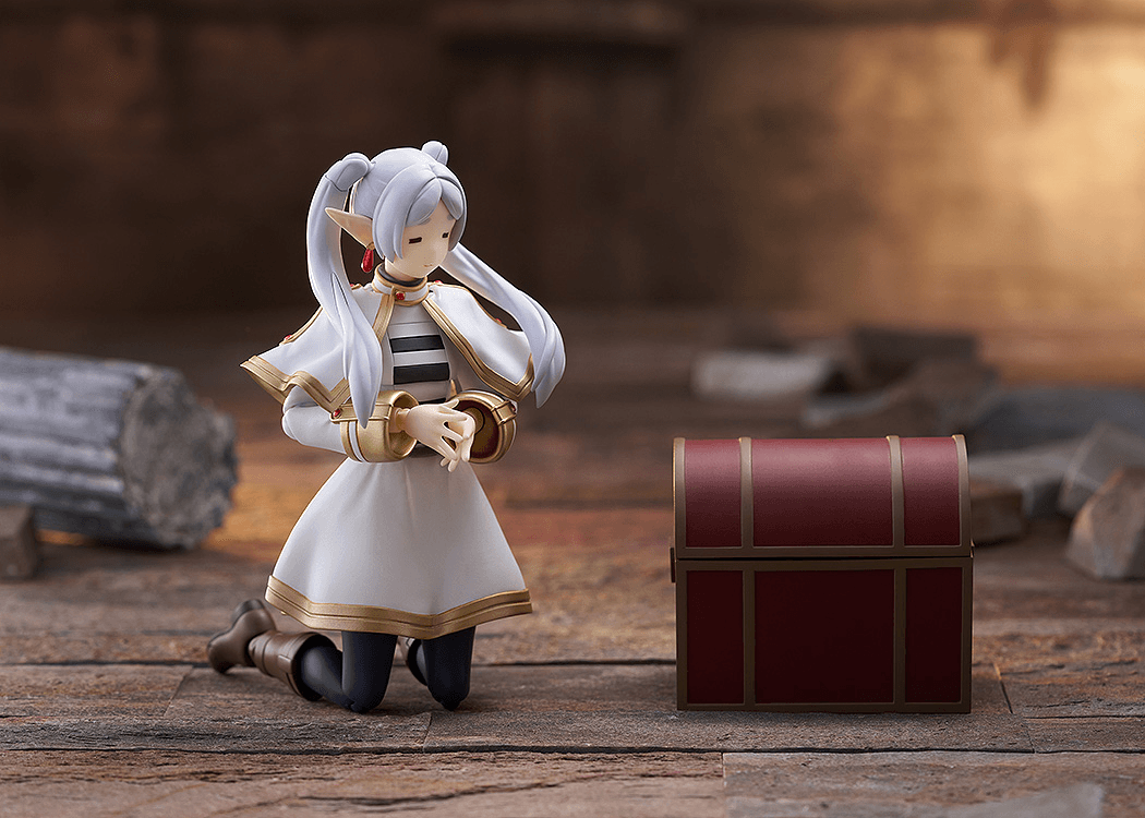 Figurine of a character with white hair and a red bow next to a treasure chest on a wooden floor.