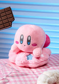 Pink plush toy with blue eyes on a checkered surface with a chocolate bar in the corner.