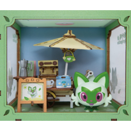 A miniature diorama model of a Pokémon Sprigatito scene, featuring a green Pokémon character in the foreground, a wooden table with a sign, a retro radio, and a yellow umbrella under a blue sky backdrop, all enclosed in a green frame.