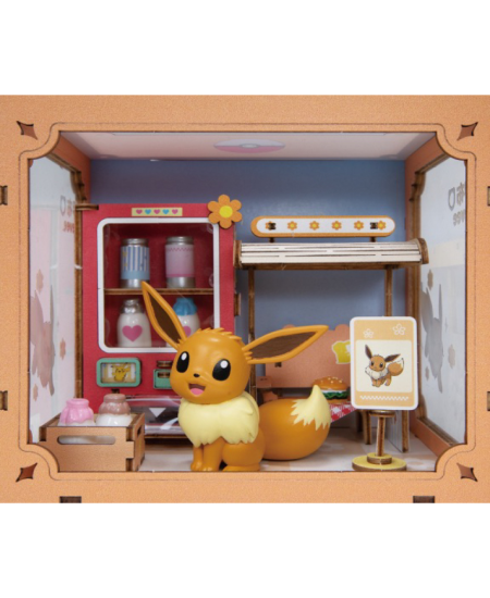 A miniature toy diorama featuring a small Eevee figurine in front of a pink vending machine and desk setup, all enclosed in a tan wooden-style frame with illustrated side panels.