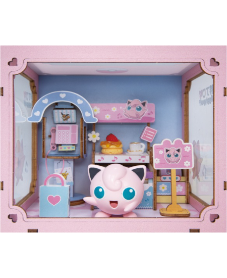 A Jigglypuff-themed miniature dollhouse display featuring a pink Jigglypuff figure in front of a pastel pink and blue room setup with shelves, a small counter, and accessories.