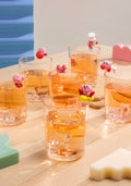 Clear glasses filled with a yellowish liquid on a wooden surface with small pink characters on top.