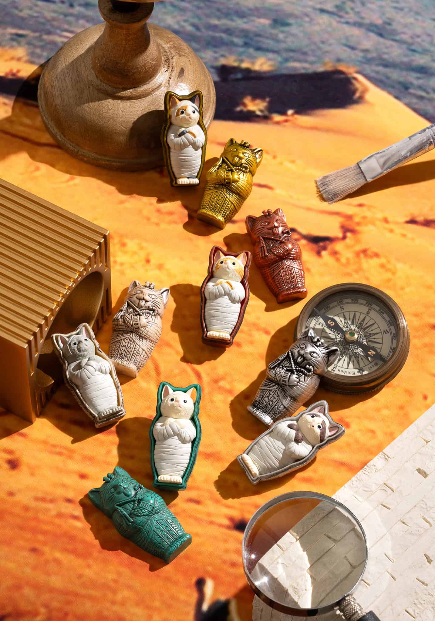 Collection of cat-shaped figurines on a wooden surface with a compass and other items.