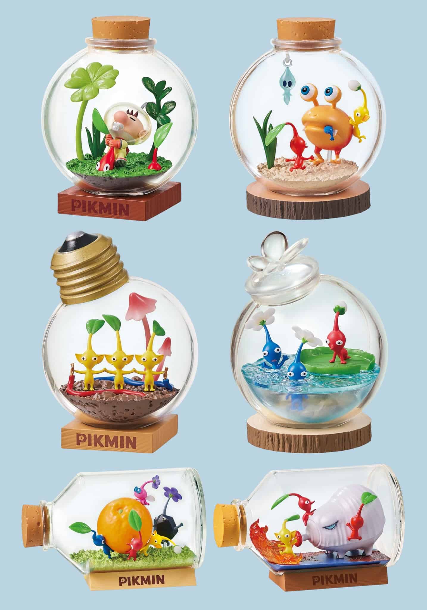 Six small decorative glass terrarium-style bottles with wooden bases and cork stoppers, each containing a different colorful miniature scene featuring Pikmin characters, displayed on a light blue background.