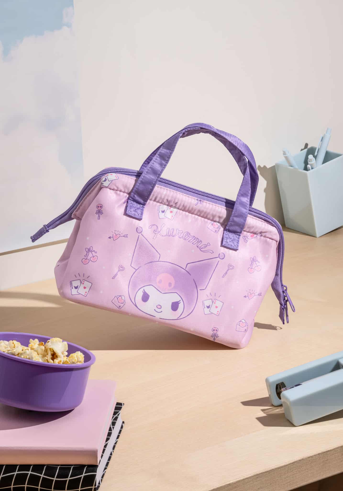 Pink handbag with cartoon character on a table with popcorn and stationery items