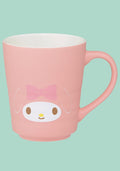 A pink ceramic mug featuring a cartoon character face with a pink bow, on a solid mint green background.