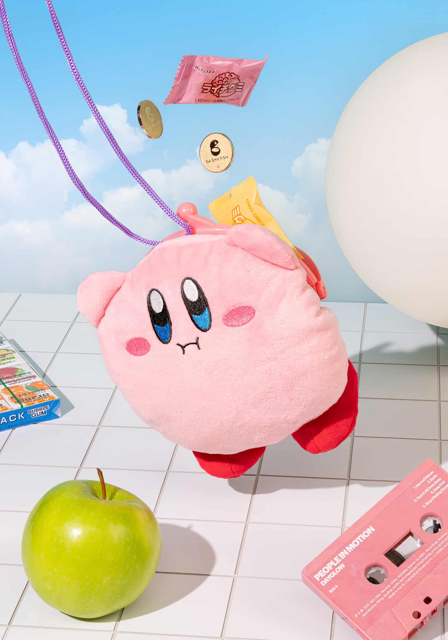 Pink plush toy with a face on a tiled floor with various items around