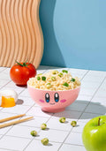 Pink cartoon-style bowl with noodles and vegetables on a tiled surface with a blue wall.