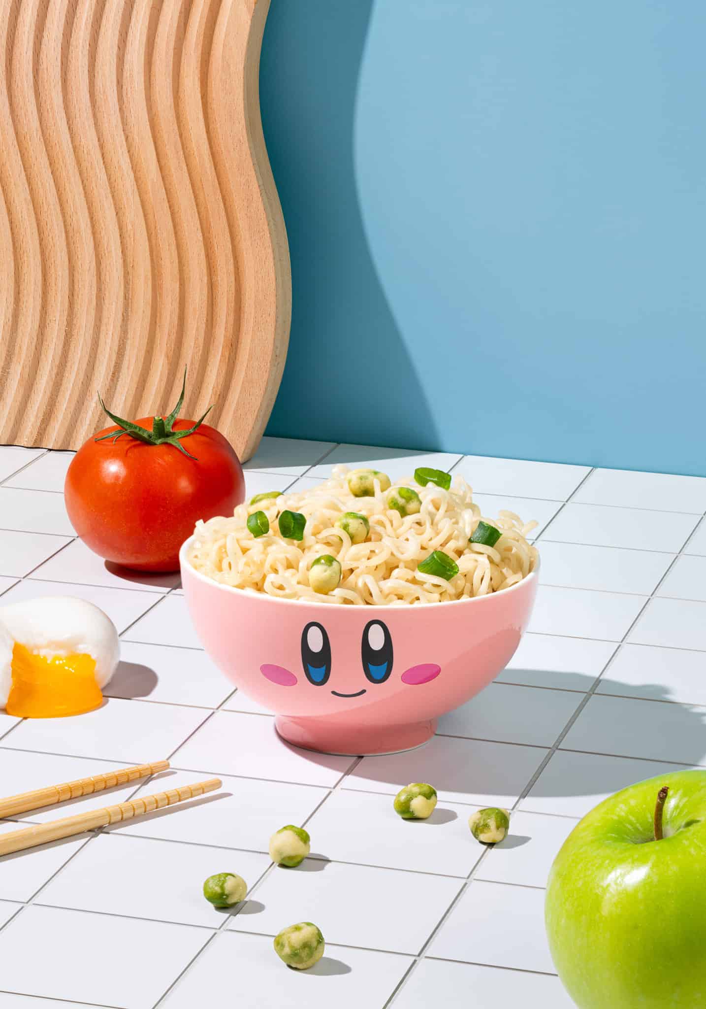 Pink cartoon-style bowl with noodles and vegetables on a tiled surface with a blue wall.