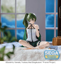 A seated anime-style figurine of a green-haired character in a white top and dark shorts, posed cross-legged on a white rug in front of a window-like backdrop. A SEGA Goods logo appears in the lower right, and copyright text for the Frieren Project is along the bottom.