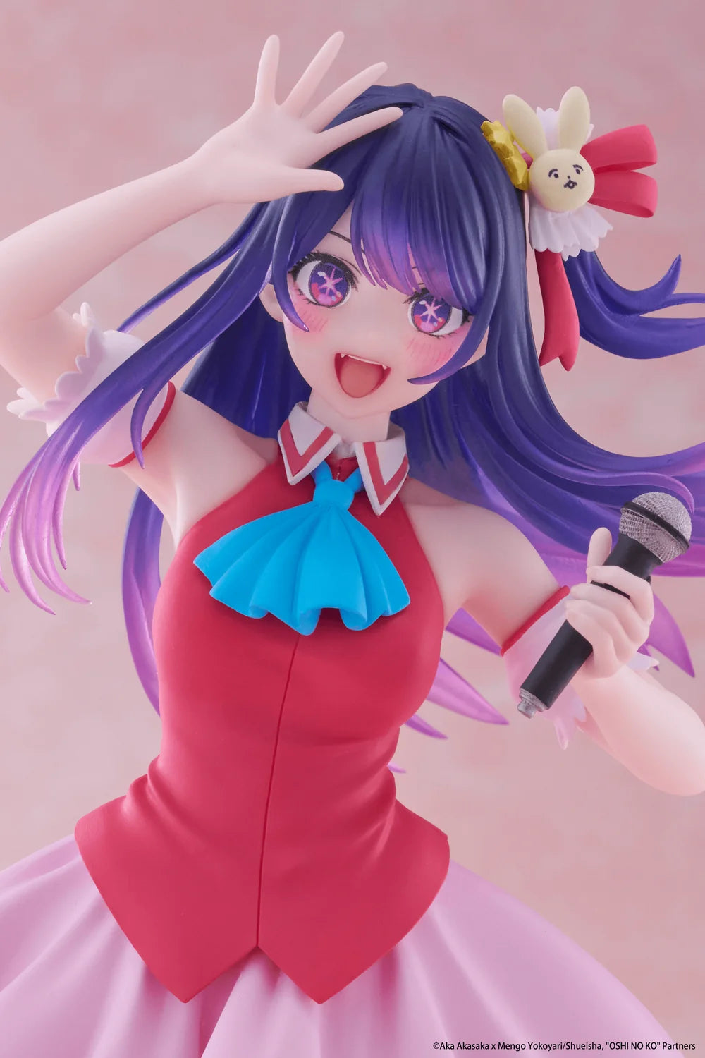 A stylized anime figurine of a purple-haired female singer in a pink and blue dress, holding a microphone against a soft pink background.