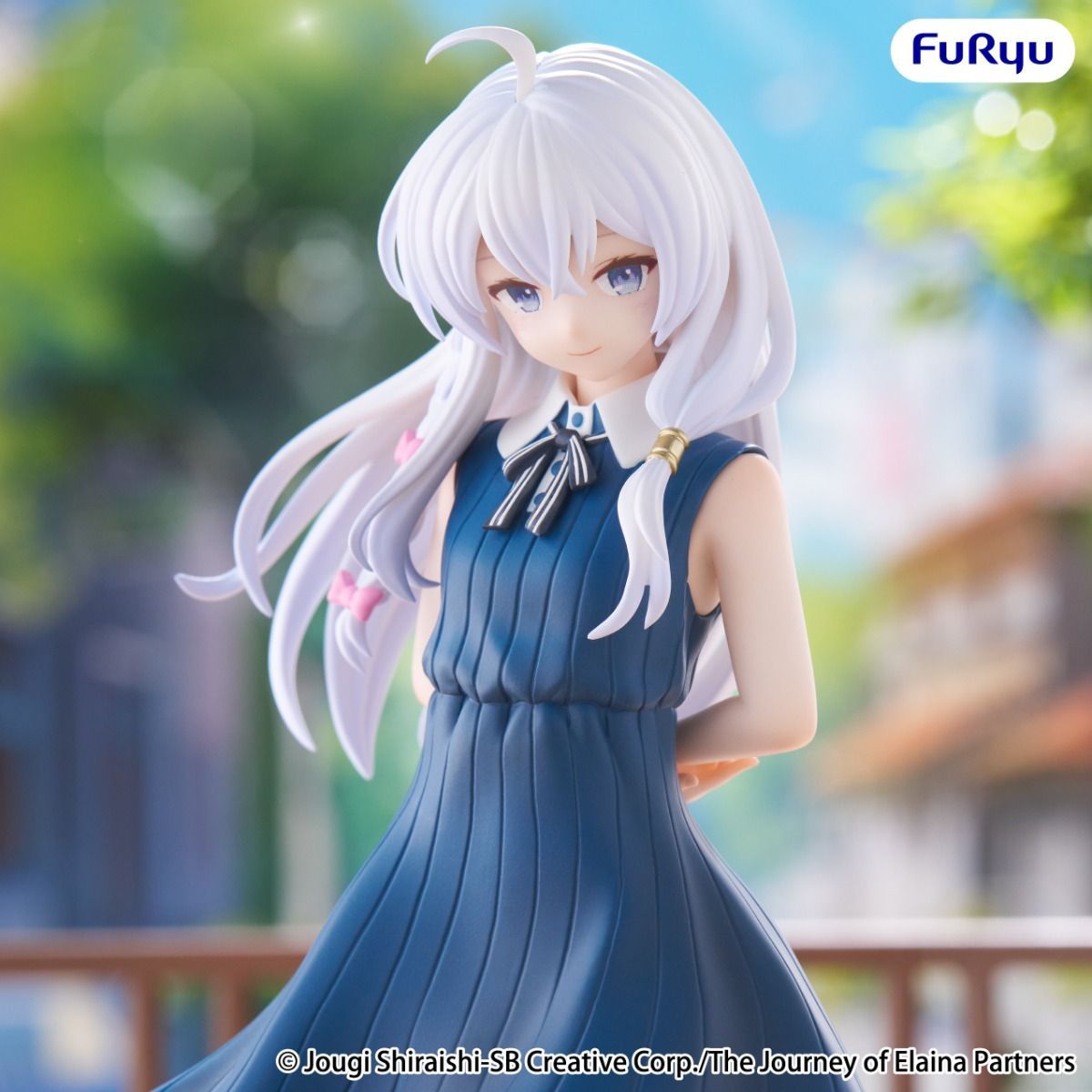Figurine of a character in a blue dress with white hair, set against a blurred outdoor background.