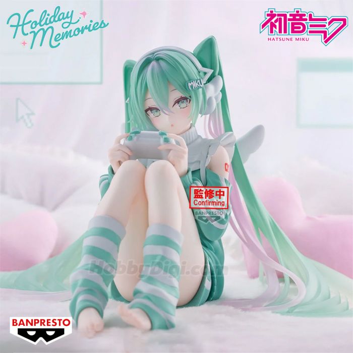 A Hatsune Miku Holiday Memories collectible figure posed sitting on a bed, holding a game controller. The figure has long mint green hair with pink and lavender streaks, cat ears, and striped thigh-high socks.