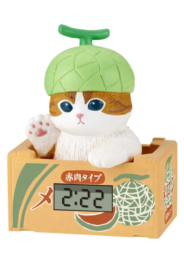 A novelty cat pig bank featuring a white and orange tabby cat wearing a green melon hat, sitting inside a melon-themed box with a digital clock display showing 2:22.