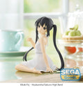 A seated anime figurine with long black twin tails wearing a white dress, posed on a tabletop in a softly blurred kitchen-like setting. A SEGA Goods logo appears in the lower right, and copyright text at the bottom reads kakifly x Houbunsha/Sakura High Band.