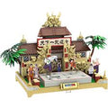 A small brick-built temple or shrine model with a brown roof, gold decorative details, a central gate, figures in front, palm trees, and a light wood base, shown on a plain white background.