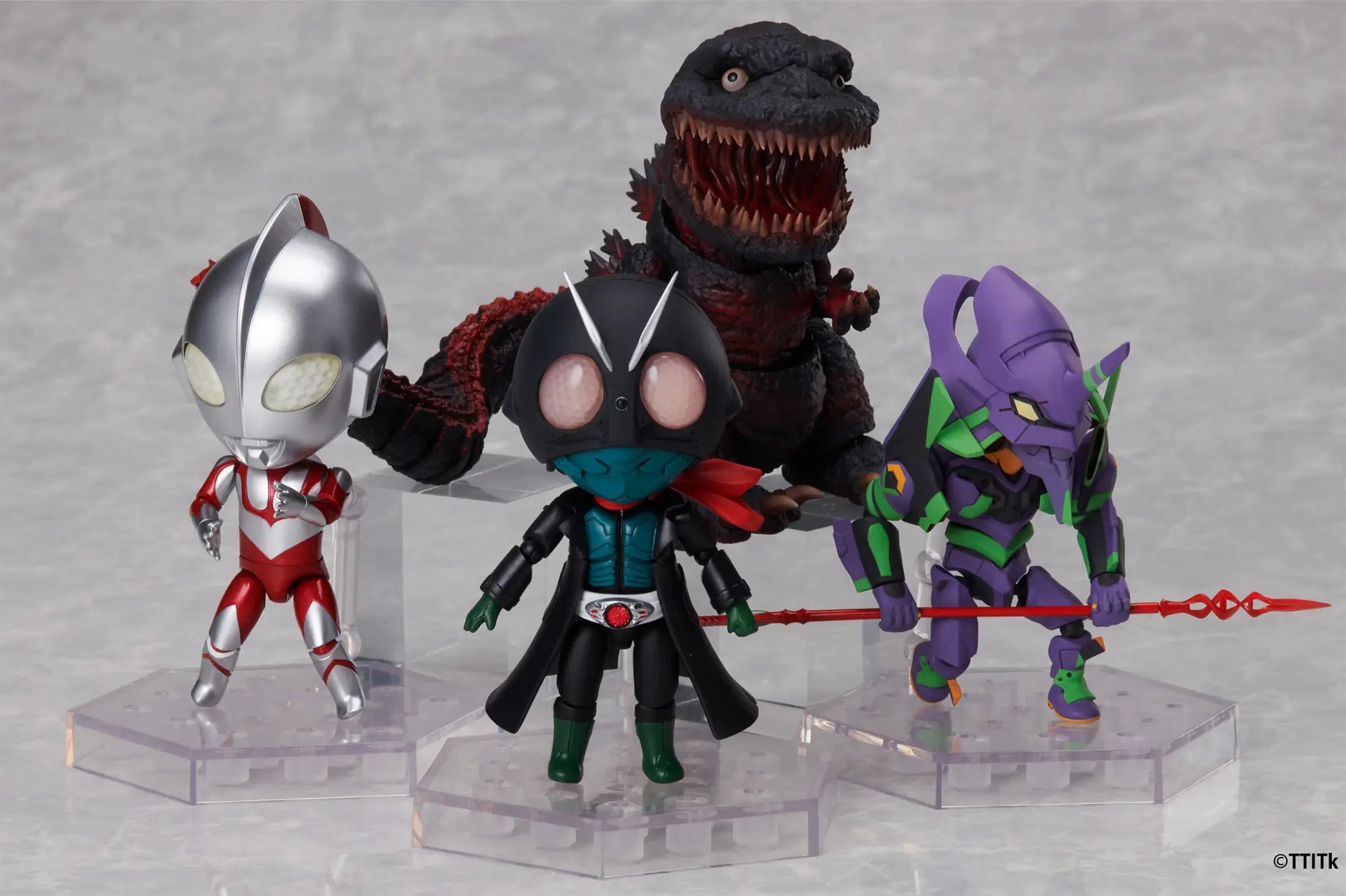 Four collectible action figures displayed on clear plastic stands against a light gray background: Ultraman, a black monster with red accents, a purple and green robot, and a central black figure with large pink eyes and a teal chest panel.