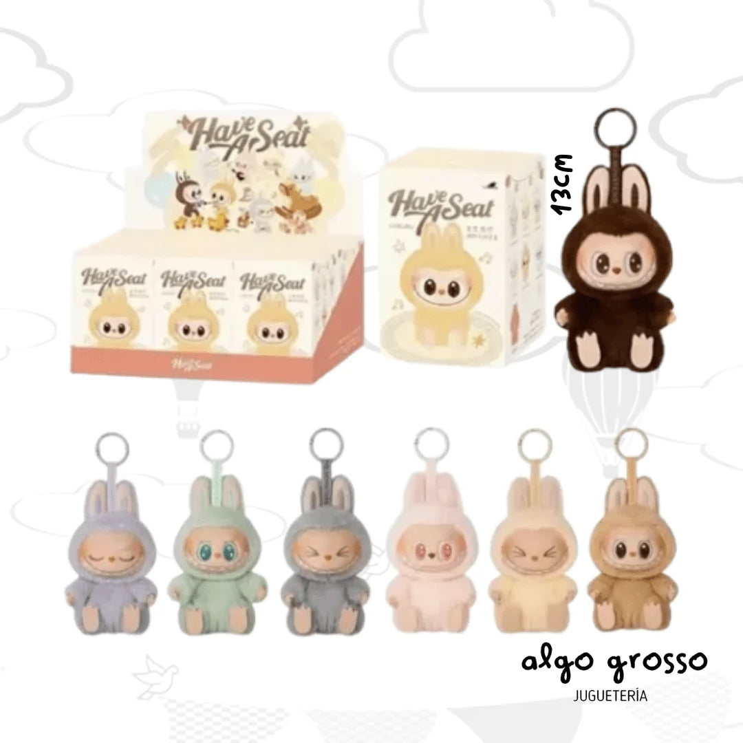 A collection of cute plush rabbit keychains by Algo Grosso, shown in multiple colors (purple, mint green, gray, pink, beige) and in their retail packaging. The image features a main dark brown plush rabbit on the right with a '13cm' size marker, and five smaller plush rabbits lined up below.
