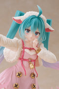 A close-up of an anime-style figurine or collectible character with bright turquoise hair, white fluffy hair accessories, pink clothing, and gold decorative accents, posed against a soft beige studio background.