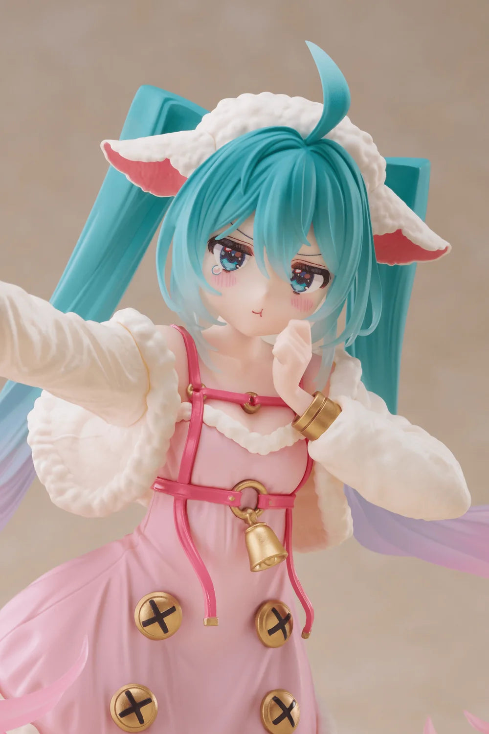 A close-up of an anime-style figurine or collectible character with bright turquoise hair, white fluffy hair accessories, pink clothing, and gold decorative accents, posed against a soft beige studio background.