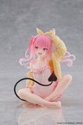 A seated anime figurine with pink hair, a pink and white outfit, a yellow animal-style jacket, and a black tail, photographed on a smooth gray surface against a gray background.