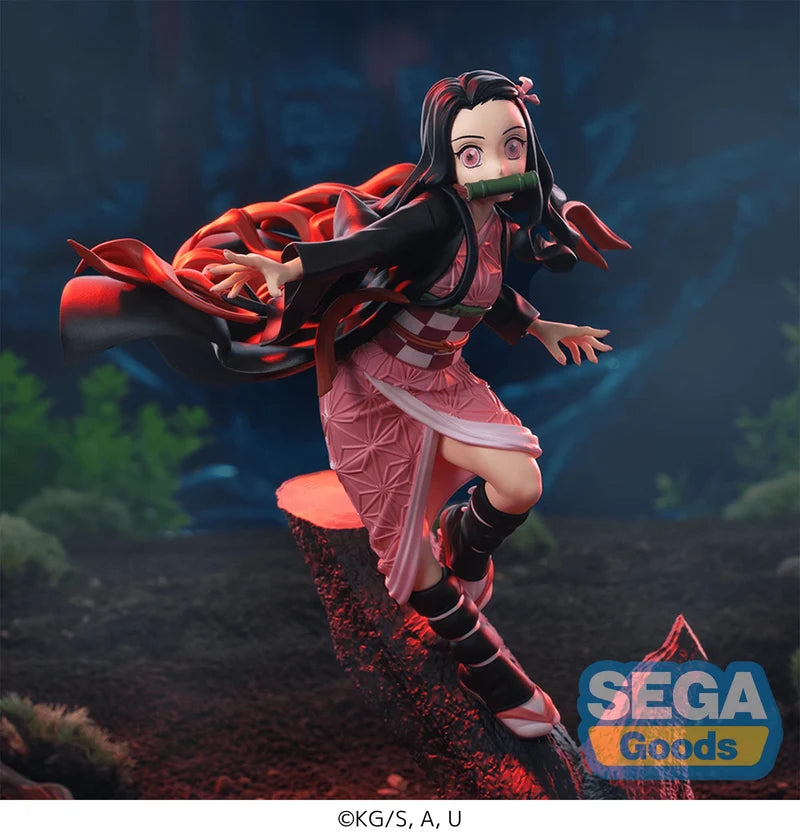 A SEGA Goods collectible figure of Nezuko Kamado from Demon Slayer, captured mid-action leaping over a log in a dark, atmospheric forest setting. The figure features her signature pink and black kimono, red hair, and green mouthpiece, with the SEGA Goods logo in the bottom right corner.