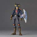 A detailed action figure of Yu-Gi-Oh! Yugi, standing on a gray studio background. He is wearing his signature blue jacket, gray pants, and brown boots, holding a white and blue card shield.